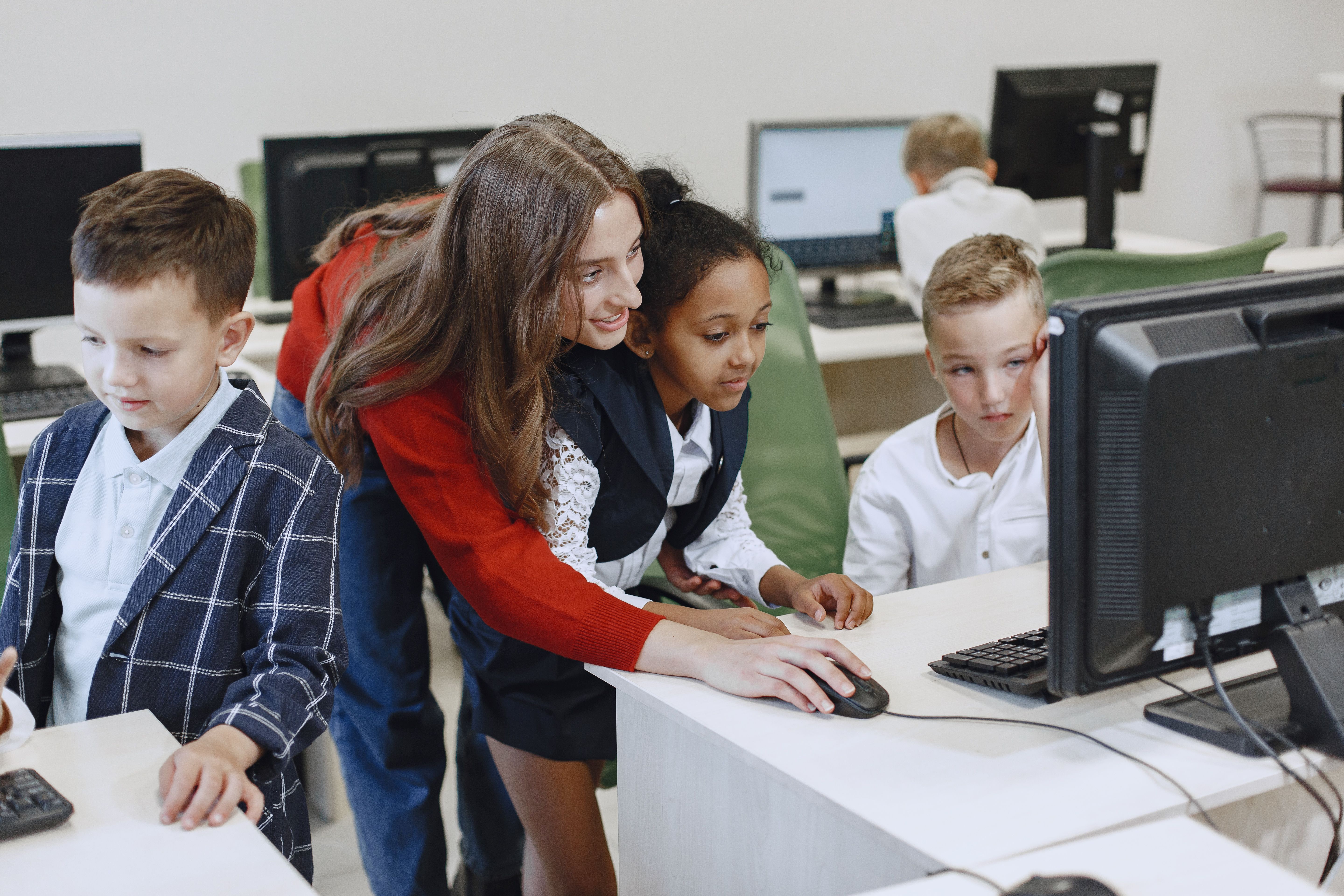 Teacher engaging diverse children in a classroom technology lesson using computers.