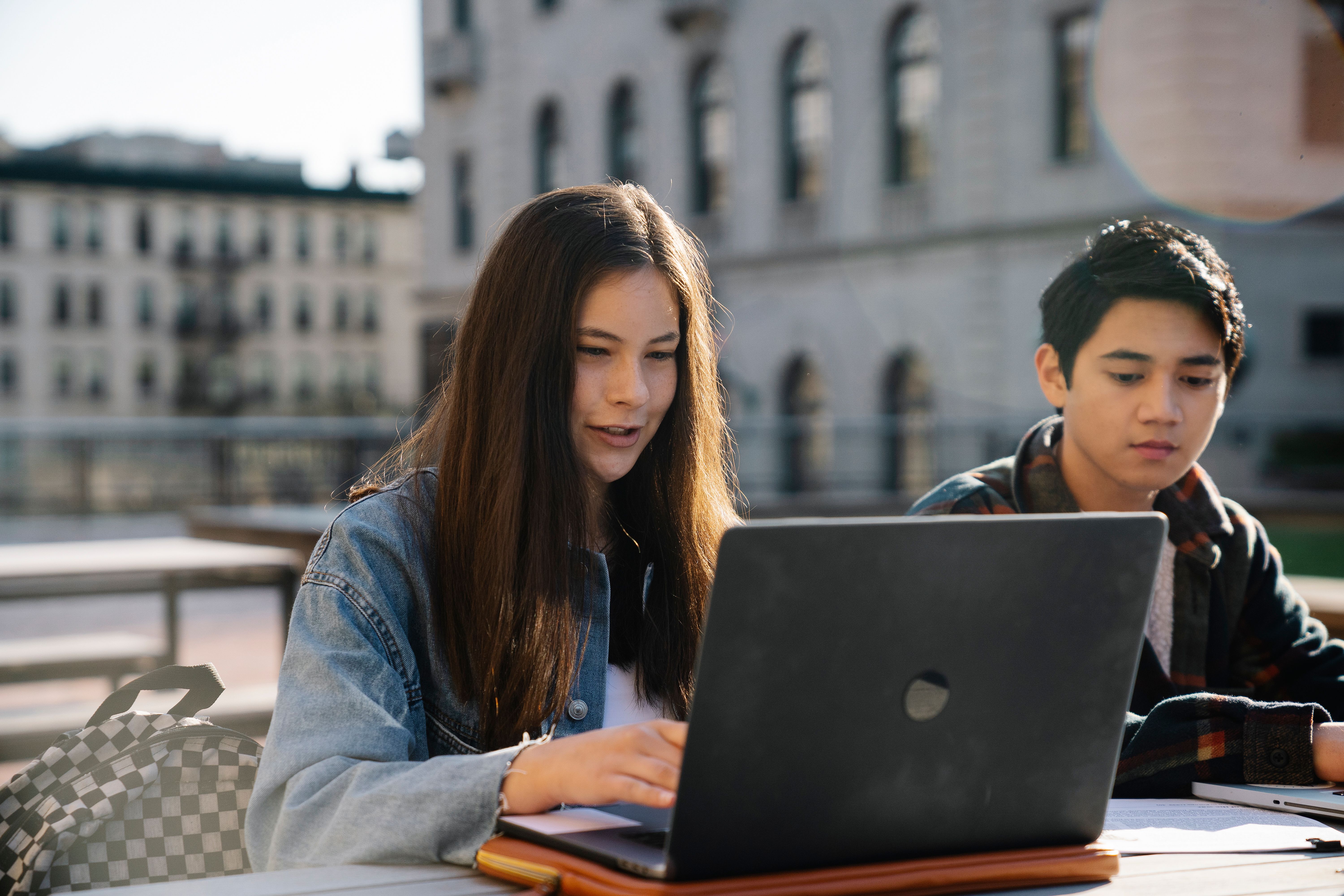 Two students collaborating on a laptop outdoors while learning together.